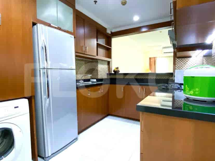 Dapur dengan lemari kayu, lemari es stainless steel, dan pemandangan area ruang tamu.