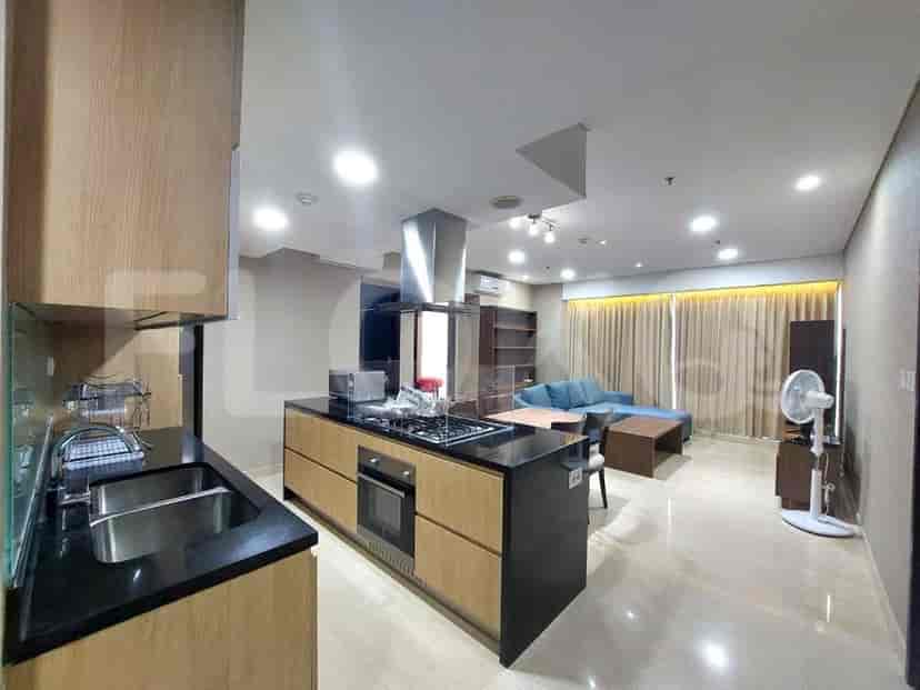 A combined kitchen and living area. The kitchen features wooden cabinets, a stainless steel chimney, and an open-plan design.