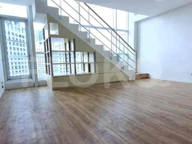 A spacious living area with a staircase, a window offering a city view, and wooden flooring.
