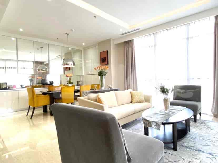 A bright living room with a cream-colored sofa, a dining area with yellow chairs, and large windows.