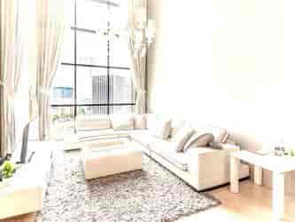 A bright living room with a white sectional sofa, large windows, and a chandelier.