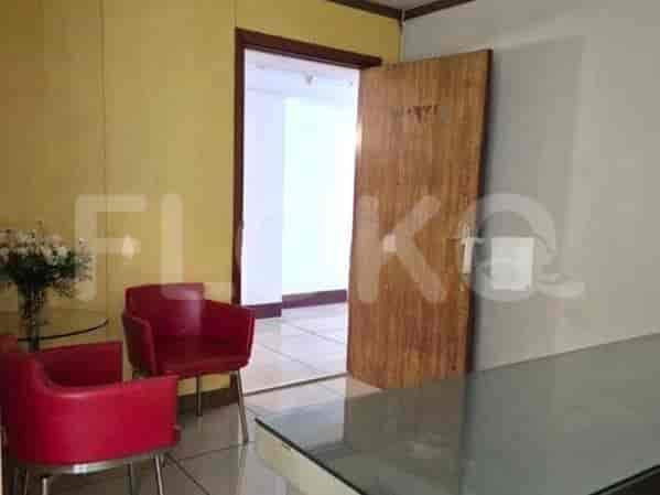 A waiting area with red chairs, a glass table, a flower vase and a door.
