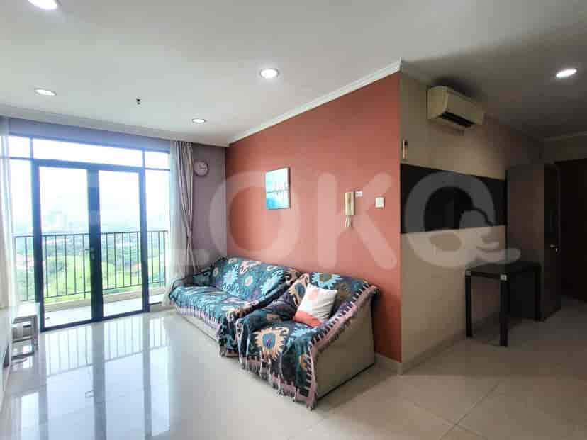 Ruang tamu dengan set sofa bermotif, pemandangan kota melalui pintu balkon, dan dinding aksen berwarna merah kecoklatan.