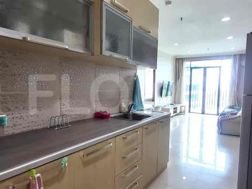 Dapur modern dengan lemari kayu, wastafel stainless steel, dan sekilas area ruang tamu.