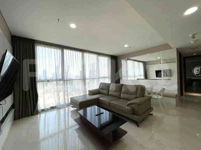 A spacious living room with an L-shaped grey sofa, wall-mounted smart TV, and large window with sheer curtains.