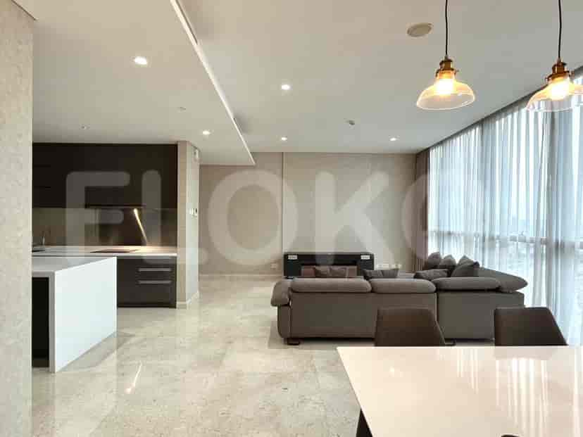 Modern apartment with open kitchen and living room featuring a grey sofa, island, and large windows.