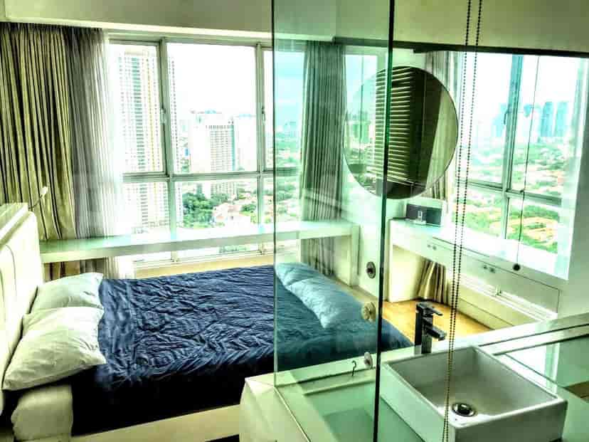 Kamar tidur cerah dengan sprei biru dan jendela besar dengan pemandangan kota.