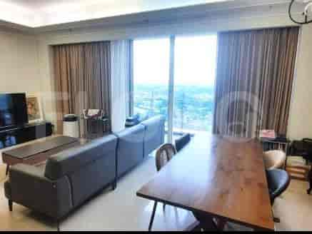 A spacious living room with an L-shaped grey sofa, wall-mounted smart TV, and large window with sheer curtains.