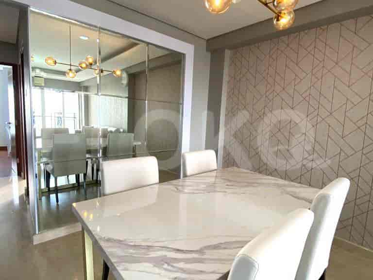 A dining area with a large marble-topped table and white chairs, adjacent to a mirror wall.
