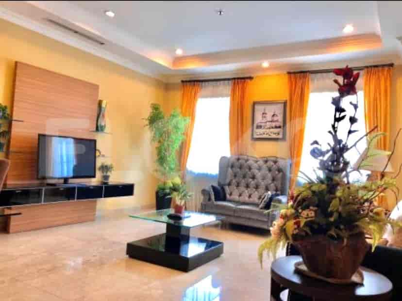 Ruang tamu yang luas dengan sofa abu-abu, TV pintar, dan jendela besar dengan gorden oranye.