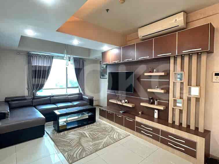 A spacious living room with an L-shaped grey sofa, wall-mounted smart TV, and large window with sheer curtains.