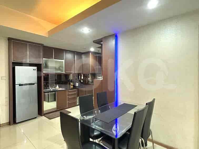A modern dining area with a glass table and a stainless steel refrigerator and kitchen cabinets.