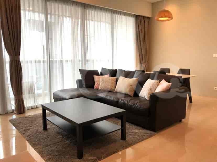 Ruang tamu dengan sofa abu-abu berbentuk L, meja kopi hitam, dan jendela besar dengan gorden tipis.