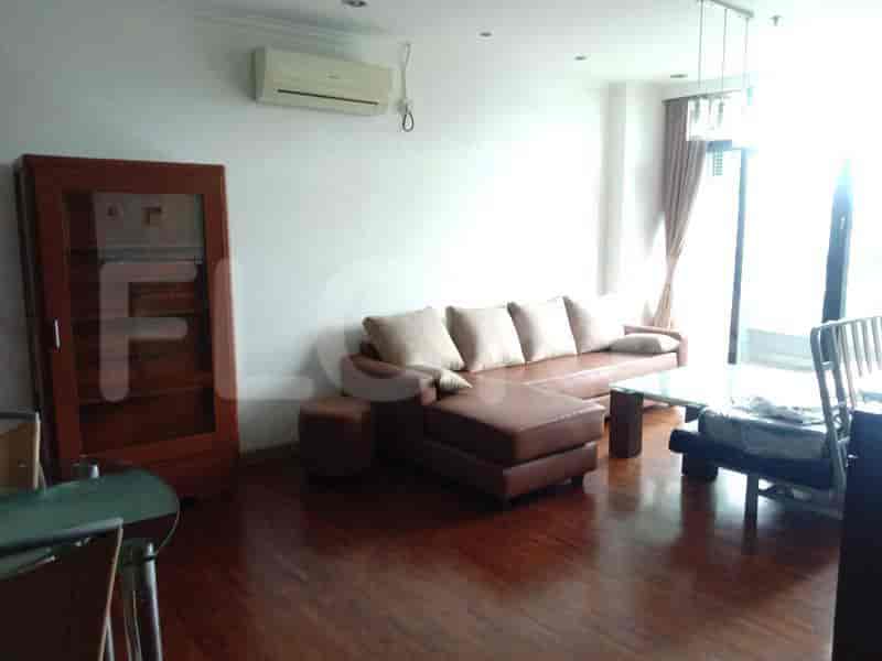 Ruang tamu yang terang dengan sofa kulit coklat, perabotan kayu, dan jendela besar.