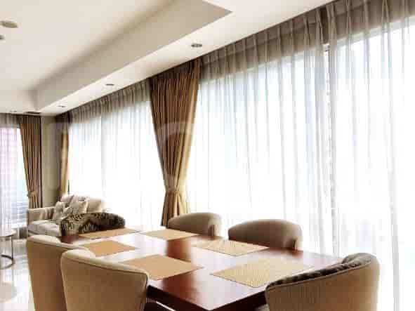 Dining area with a wooden table and chairs, large windows with sheer curtains.