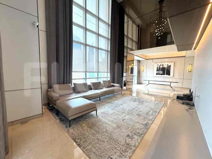 A luxury living room with a grey L-shaped sofa, large windows with sheer curtains, and a cityscape view.