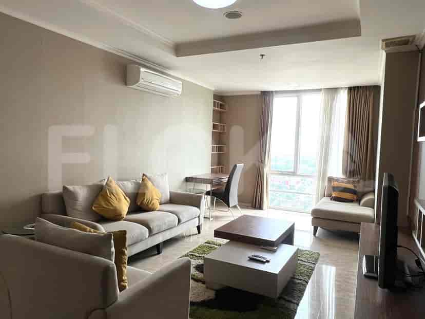 A spacious living room with an L-shaped grey sofa, wall-mounted smart TV, and large window with sheer curtains.