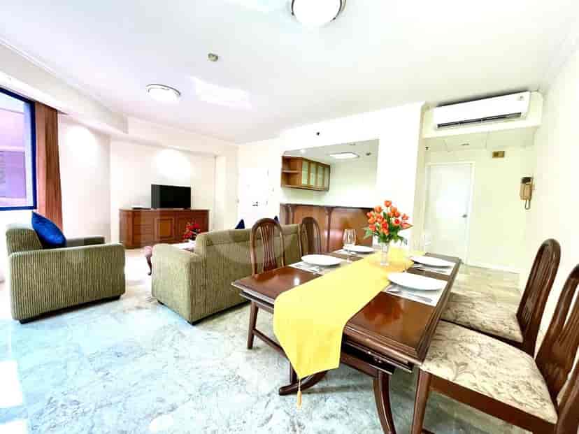 The combined living and dining area with a wooden dining table, chairs, and kitchen in the background, featuring light grey marble flooring.