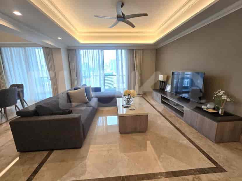 A spacious living room with an L-shaped grey sofa, wall-mounted smart TV, and large window with sheer curtains.