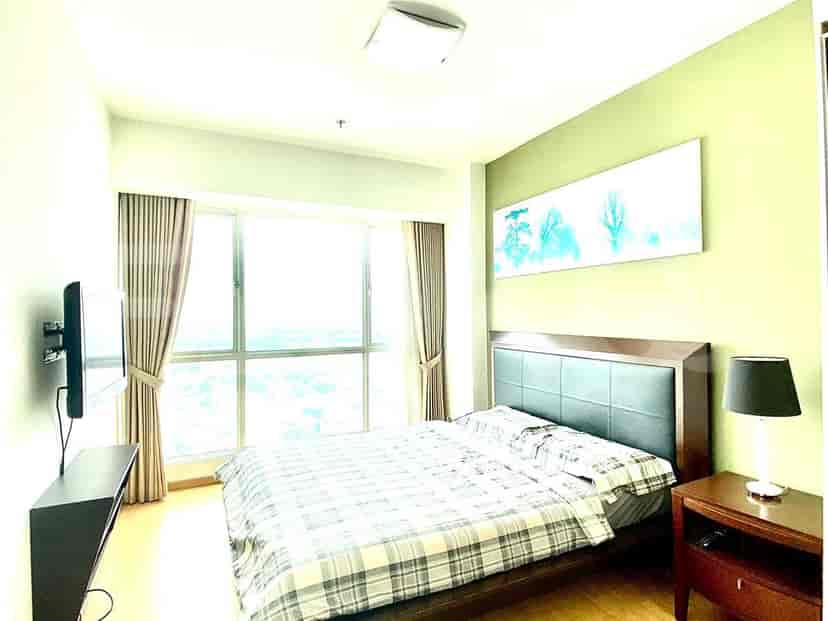 A well-lit bedroom with a bed, TV, and artwork.