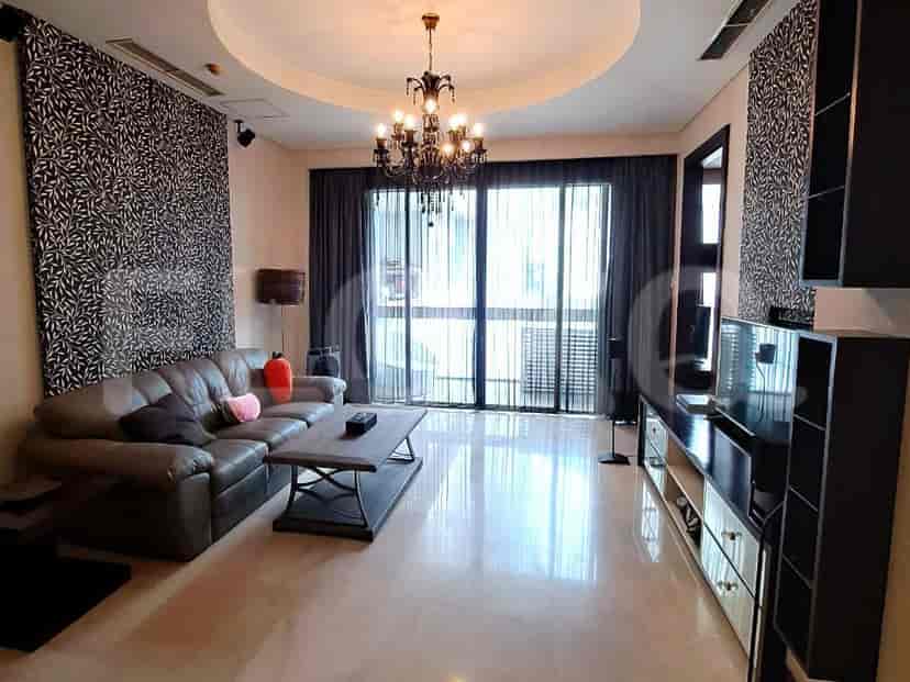 A spacious living room with an L-shaped grey sofa, wall-mounted smart TV, and large window with sheer curtains.