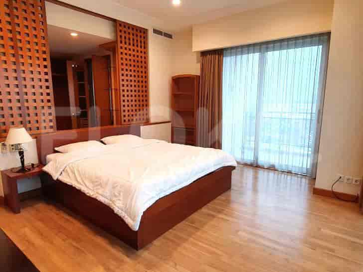 A cozy bedroom featuring a bed, wooden accents, and large windows with sheer curtains.
