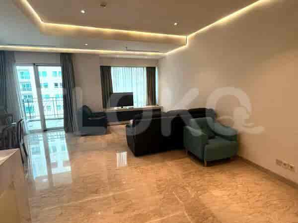 A spacious living room with an L-shaped dark sofa, an armchair, and a large window with sheer curtains.