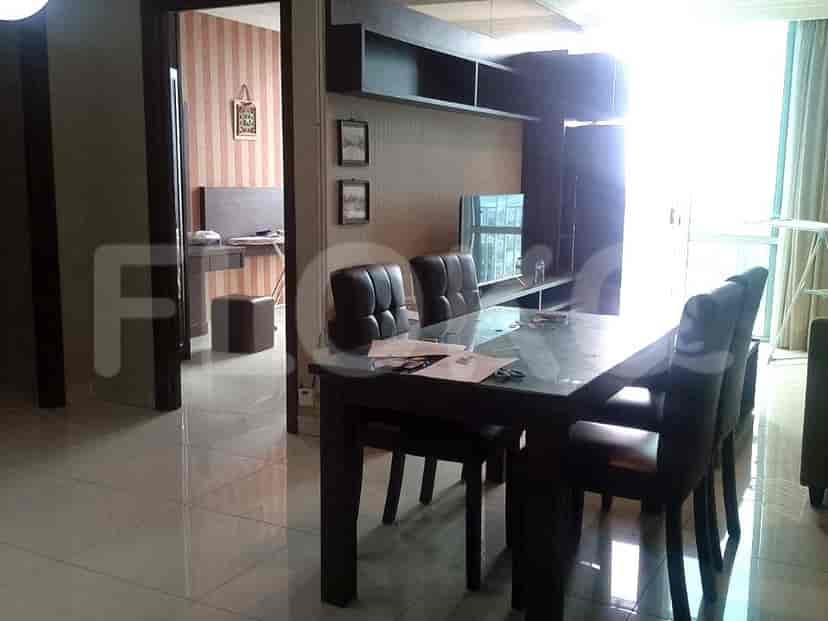 A dining room with a glass-top dining table and four dark leather chairs, adjacent to a living area with a TV console.