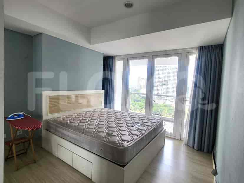 A bedroom with a queen-sized bed, light wooden flooring, and a view of the city.
