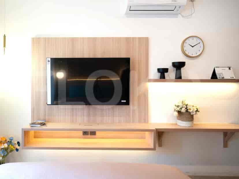 A bedroom with a TV area including a wooden shelf, a smart TV, and decorative elements.
