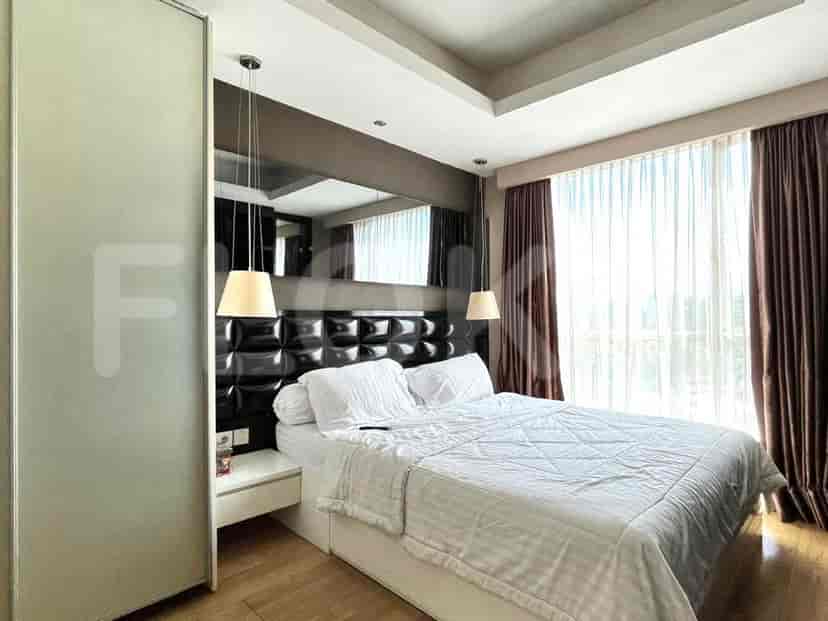 A bedroom with a bed, bedside table, and large windows with curtains.