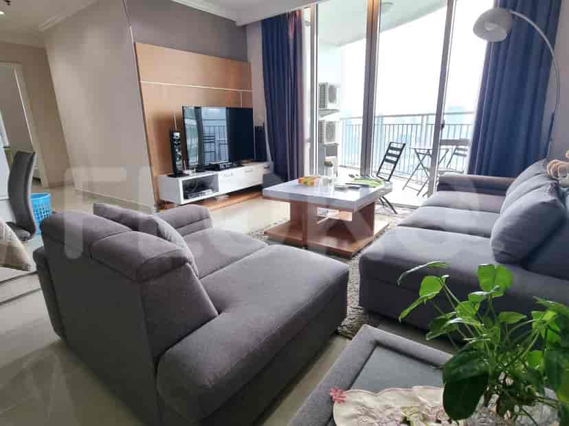 A modern living room featuring a grey L-shaped sofa, a TV, and a balcony with a city view.