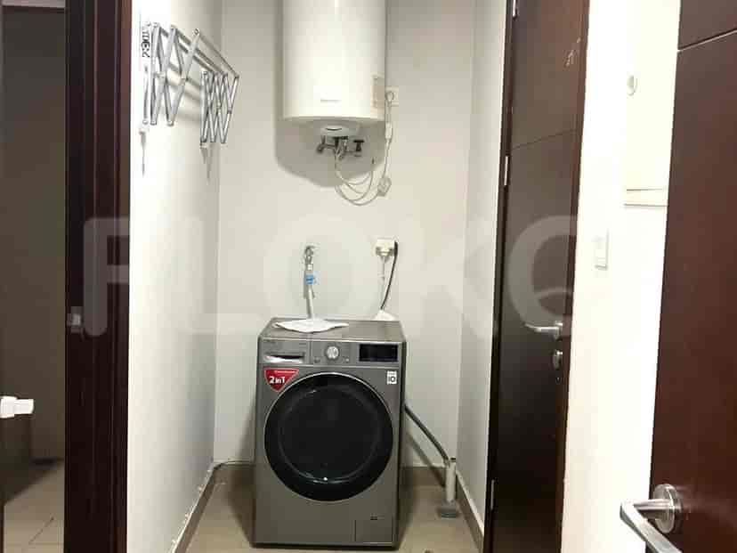 Ruang cuci kecil dengan mesin cuci, pemanas air, dan rak pengering.