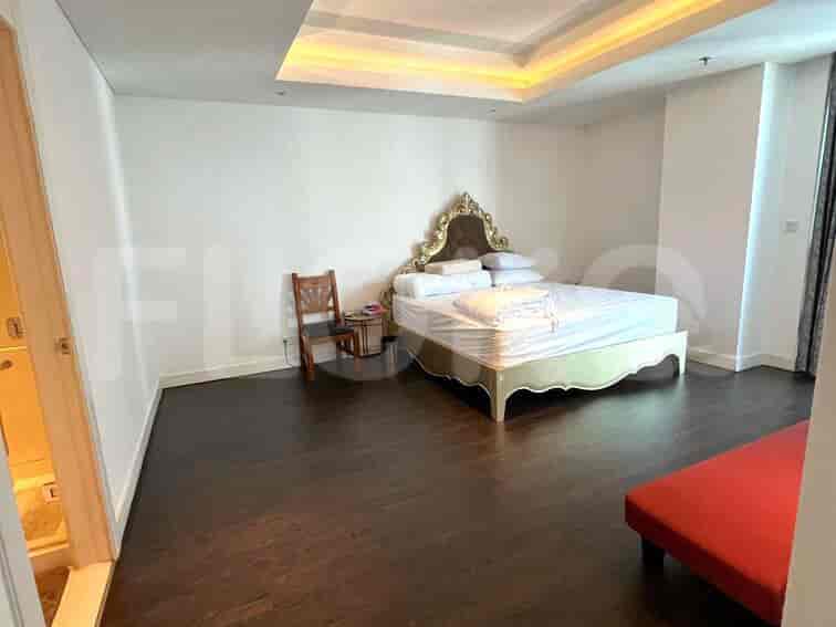 Kamar tidur luas dengan tempat tidur ukuran king, lantai kayu keras, dan bangku merah.