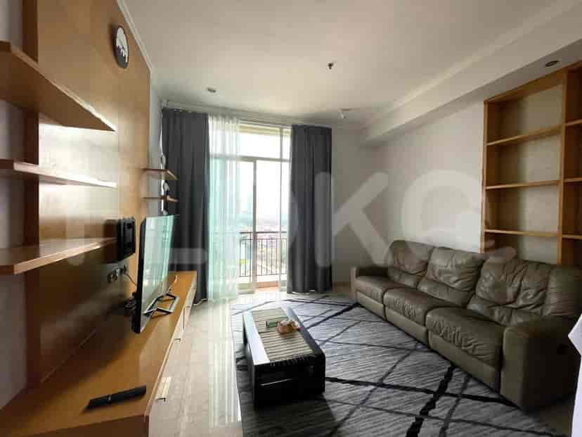 A spacious living room with an L-shaped grey sofa, wall-mounted smart TV, and large window with sheer curtains.