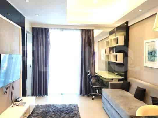 A living room with a grey sofa, a wall-mounted TV, and a desk area.