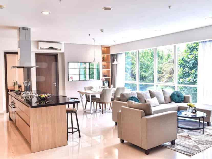 A combined living and kitchen area with a kitchen island, a living area with a grey sofa, and large windows with a view.