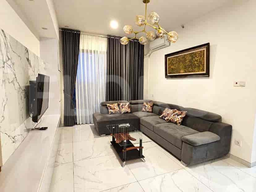 Ruang tamu modern dengan sofa abu-abu berbentuk L, TV yang dipasang di dinding, dan jendela besar.
