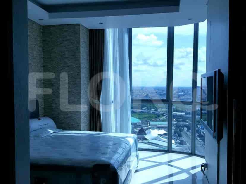 A modern bedroom with large windows offering a city view, featuring a bed and a flat-screen TV.