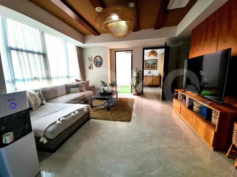 Ruang tamu yang luas dengan sofa abu-abu berbentuk L, TV pintar yang dipasang di dinding, dan jendela besar.