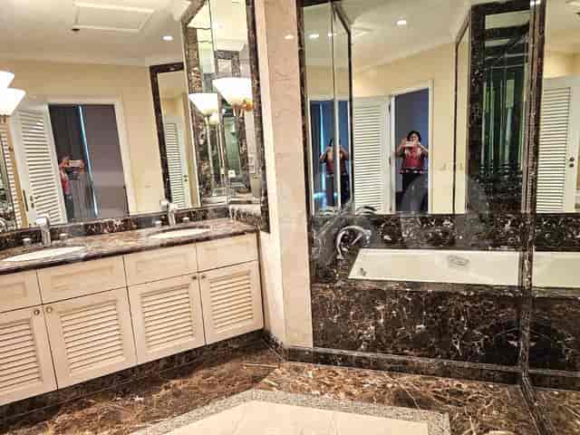 A luxurious bathroom with a double vanity, marble countertops and walls, and a bathtub.