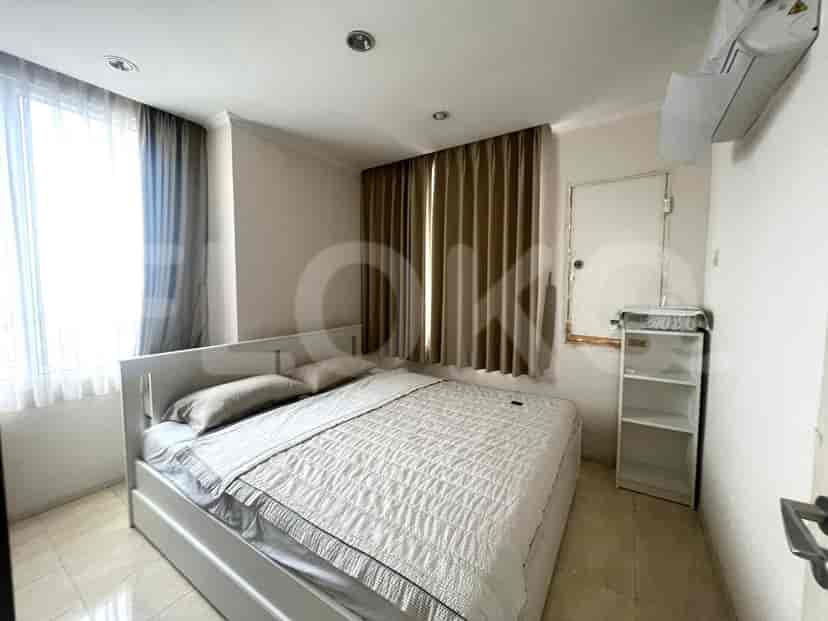 Kamar tidur dengan tempat tidur ukuran queen, jendela besar dengan tirai, dan rak buku kecil.