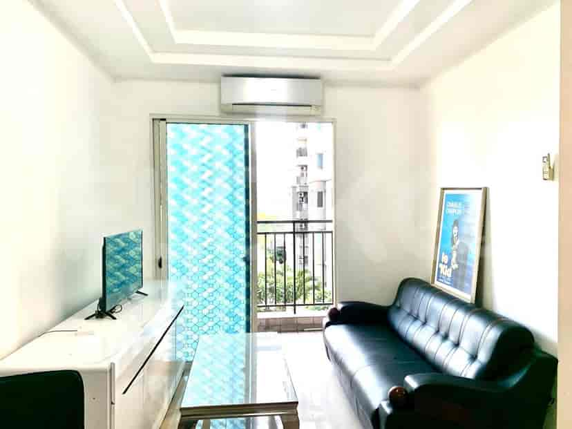 A living room with a black leather sofa, a glass coffee table, a television on a white console, and a large window with a patterned film.