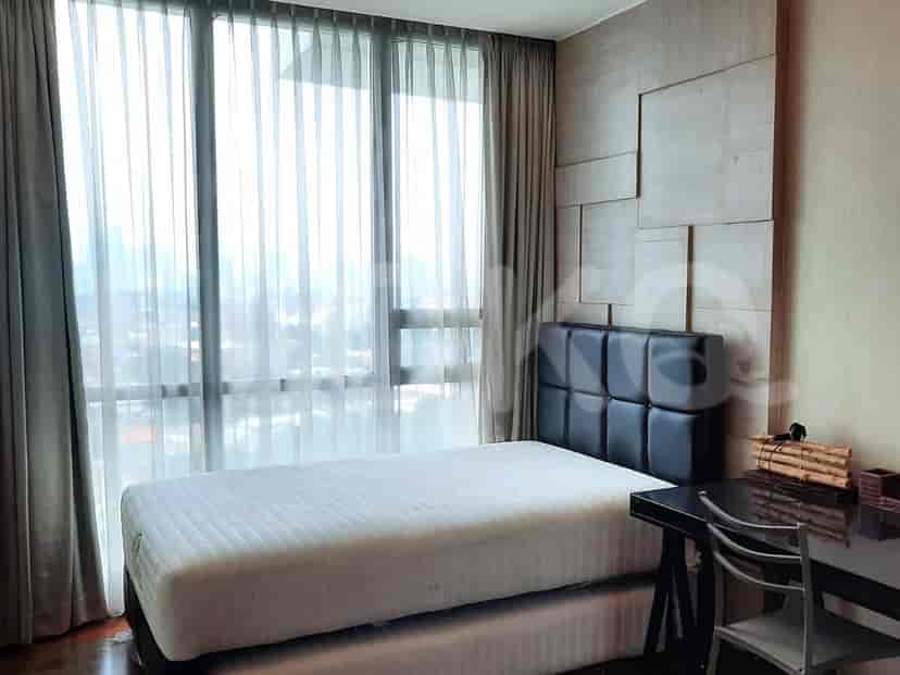 A bedroom with a single bed, a desk, and large windows with curtains.