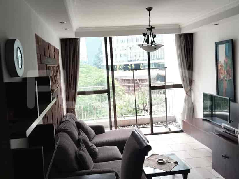 A living room with a large sectional sofa facing a window with a city view, and a TV console on the right.