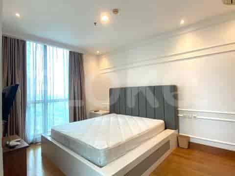 A bedroom with a large bed, a TV console, and a window with sheer curtains.