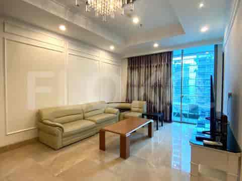 A living room with a beige sectional sofa, a coffee table, a TV console, and large windows with draped curtains.