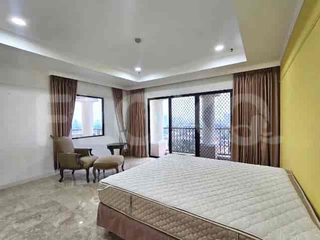 A bedroom with a large bed, a chair with an ottoman, and large windows with brown curtains.
