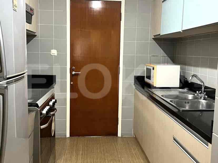 A compact kitchen with grey tiled walls, wooden cabinets, a sink, a microwave, and a refrigerator.
