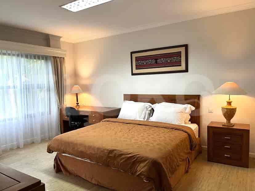 A bedroom with a queen-size bed, a wooden desk and chair, bedside tables with lamps, and a large window with curtains.